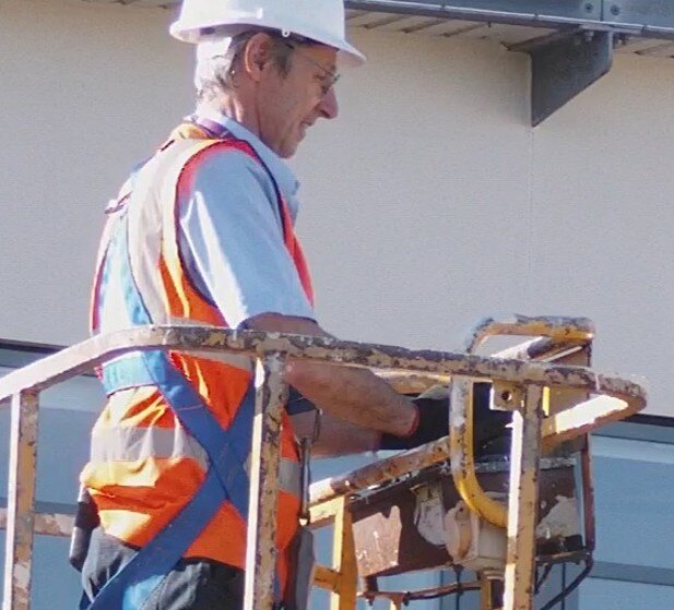Gary Brett on site in hard hat and hi-vis, working from a boom lift